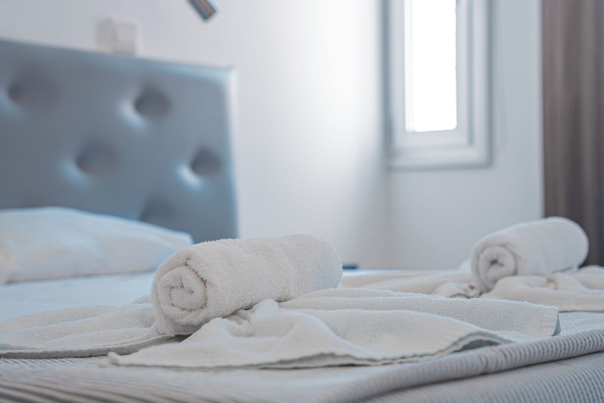A neatly made bed with rolled white towels and a tufted headboard.