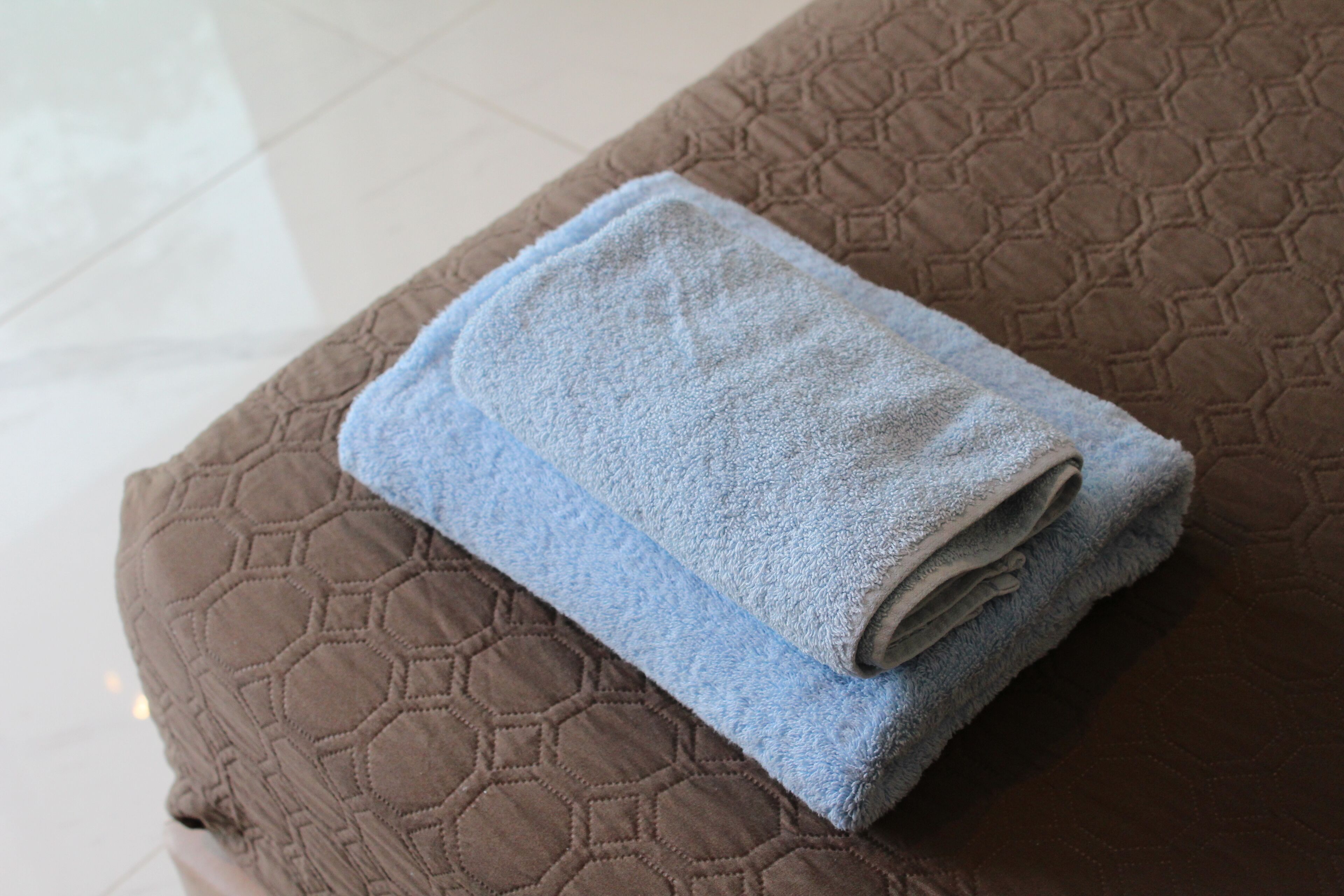 A neatly folded blue towel on a brown quilted ottoman.