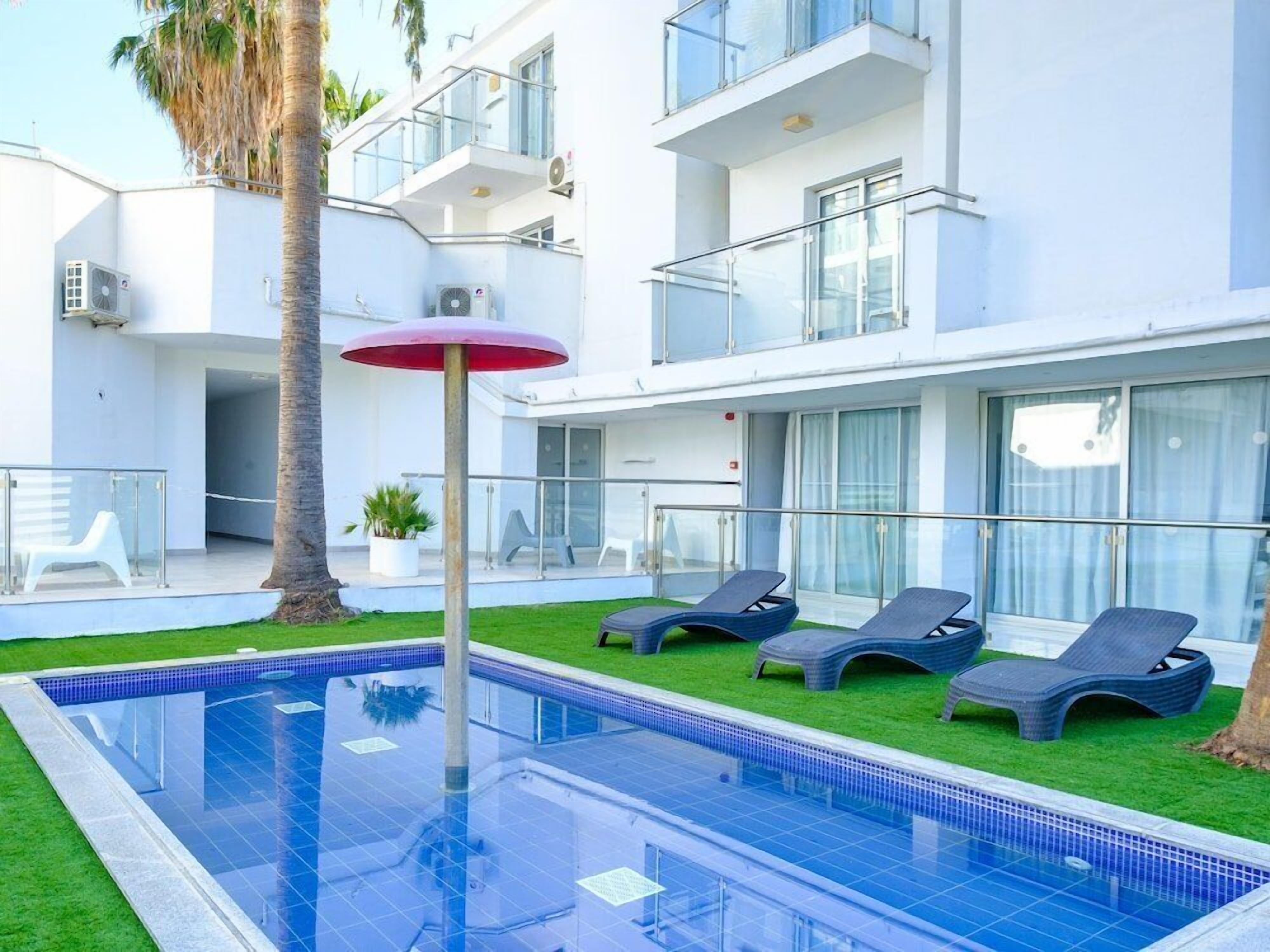 A modern hotel with a swimming pool, lounge chairs, and a palm tree.