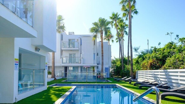 A swimming pool with a tiled edge, surrounded by a well-maintained lawn and palm trees. - Rio Gardens Aparthotel (Ayia Napa)