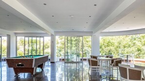 A spacious indoor area with a pool table, comfortable seating, and large windows offering a view of greenery. - Rio Gardens Aparthotel (Ayia Napa)