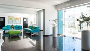 A modern lobby with teal sofas, a green ottoman, a world map on the wall, and a large potted plant. - Rio Gardens Aparthotel (Ayia Napa)