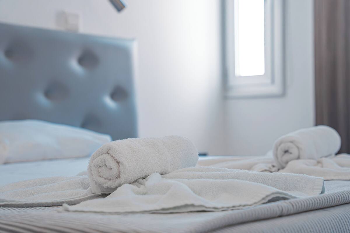 A neatly made bed with rolled white towels and a tufted headboard.