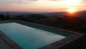 Una piscina con vista a la puesta de sol y colinas al lejano.