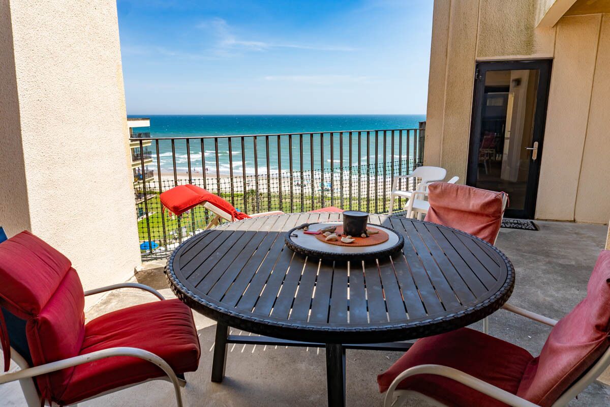 A balcony with a round table, red cushioned chairs, and a view of the ocean.