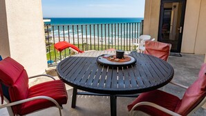 Ein Balkon mit einem runden Tisch, roten Sitzgelegenheiten und Blick aufs Meer.