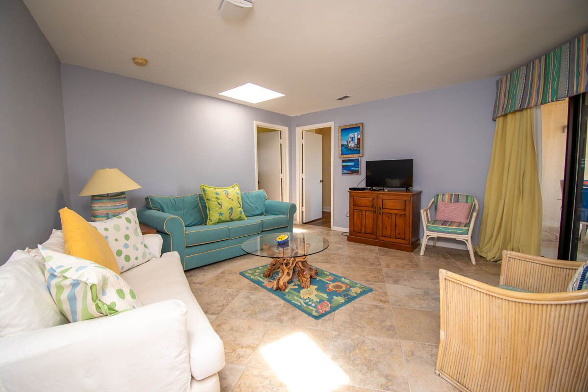 A living room with a sofa, a coffee table, a television, and a wicker chair.