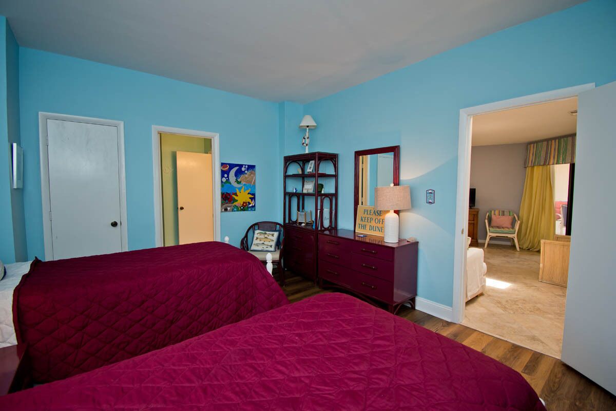 A bedroom with two beds, a dresser, a mirror, and a door leading to another room.