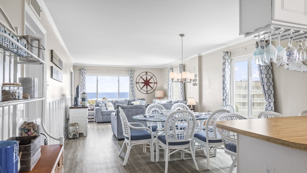 Een moderne keuken met witte kasten, een eethoek met een ronde tafel en stoelen, en een groot raam met uitzicht op de oceaan.