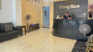 Un área de recepción con un mostrador negro, una mujer sentada detrás y un reloj en la pared.