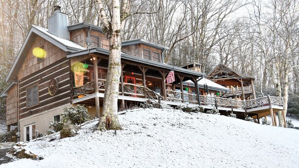 Ein blockhausartiges Gebäude mit Veranda und mehreren Ebenen, umgeben von schneebedeckten Bäumen.