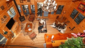 Ein Blockhaus-Interieur mit Kamin, Holzmöbeln, einer Chandelierleuchtre und Blick ins Freie.
