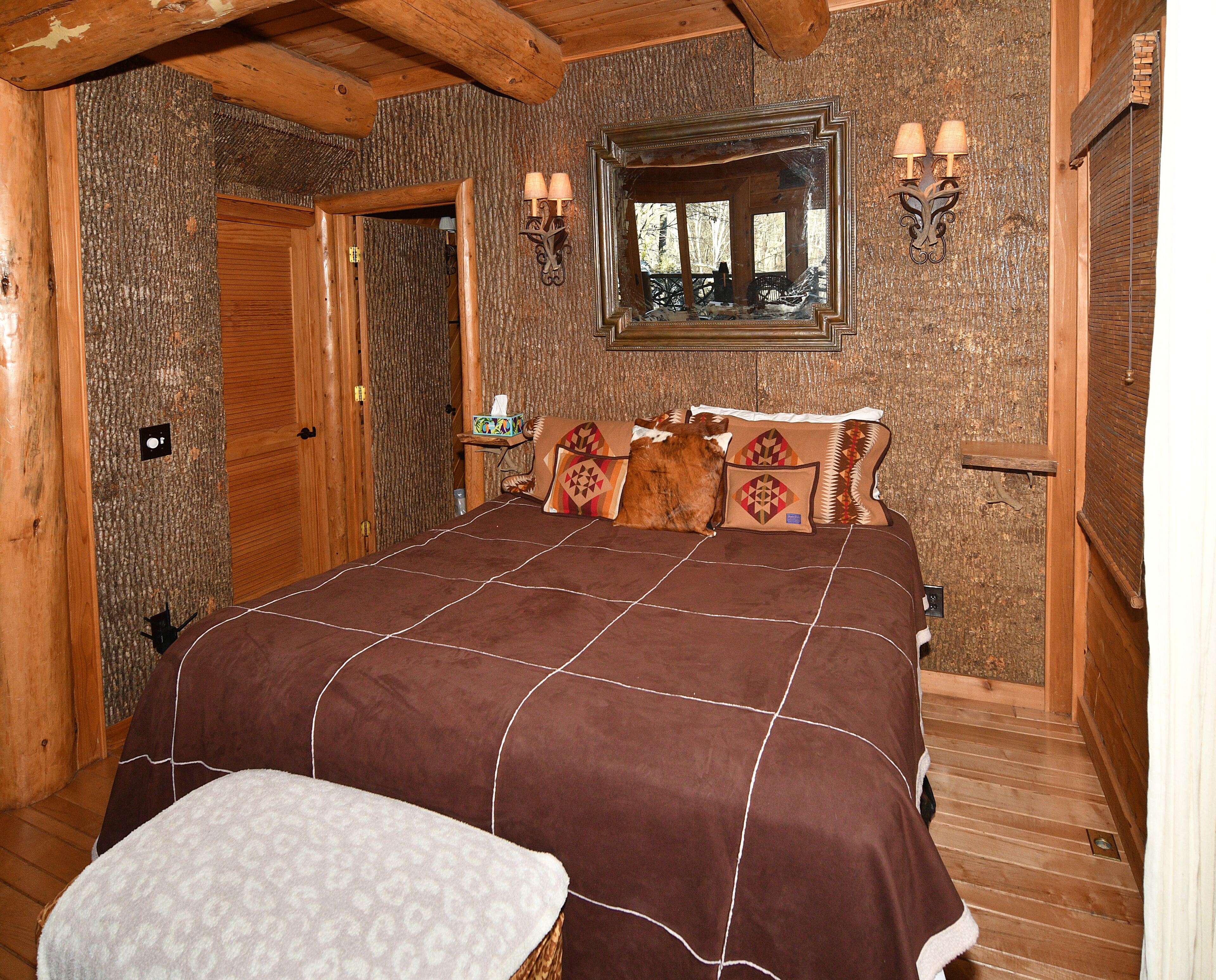 Ein Schlafzimmer in einer Holzhütte mit einem großen Bett, einem Nachttisch, einem Spiegel und einer Holztür.
