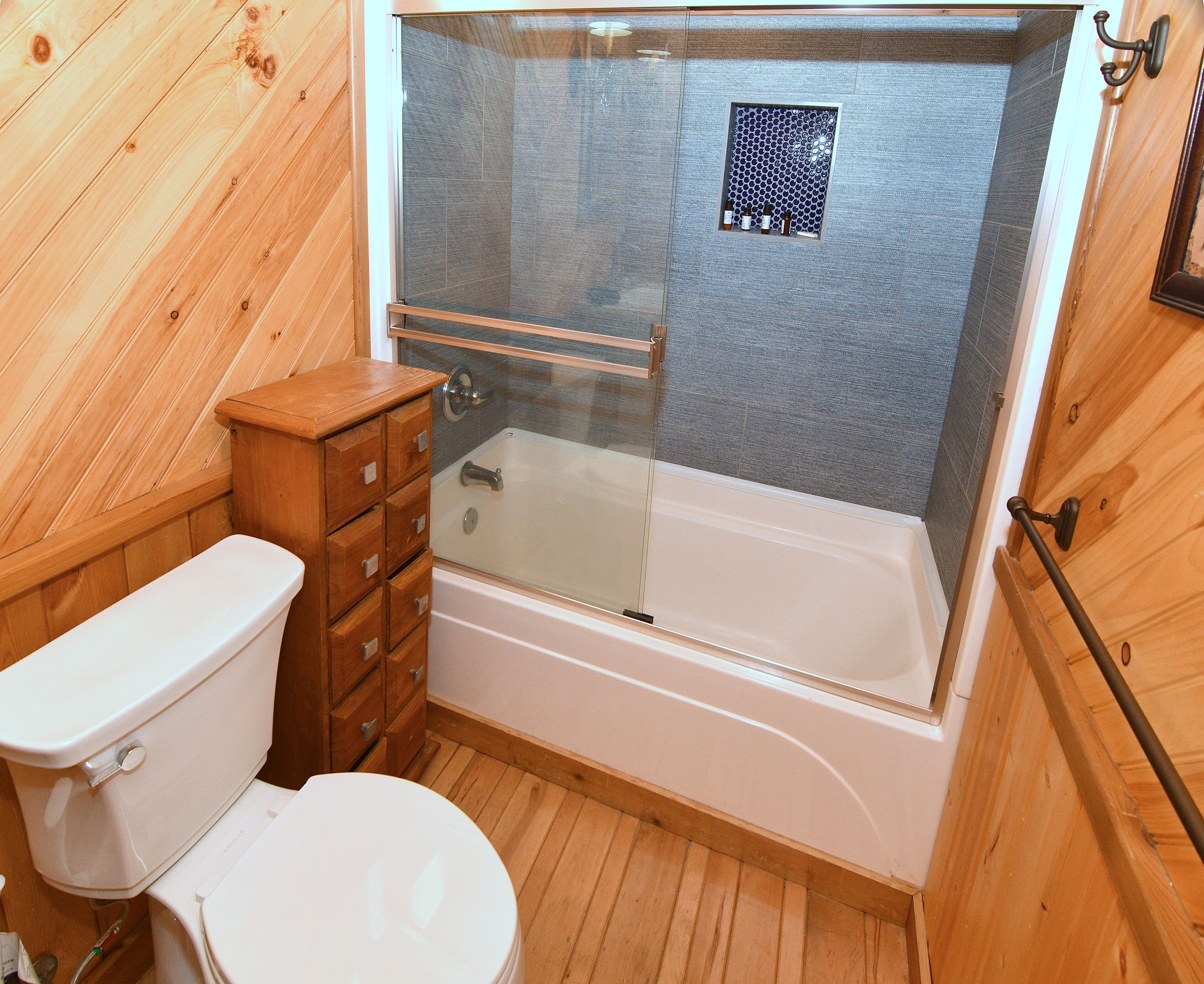 A wooden-paneled bathroom with a glass-enclosed shower, a white toilet, and a wooden cabinet.