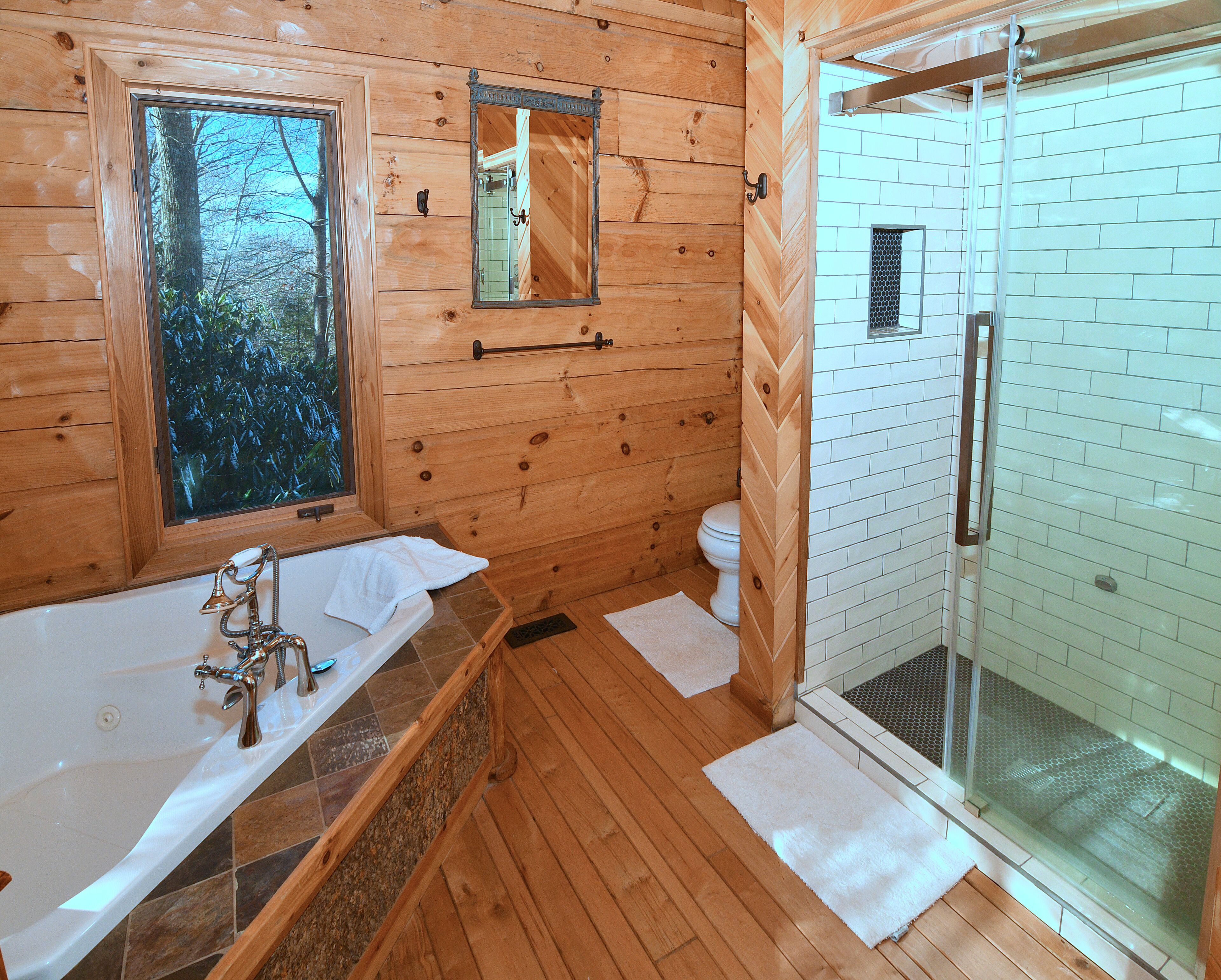 A wooden cabin bathroom with a bathtub, a toilet, and a glass-enclosed shower.
