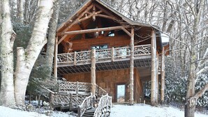 Une cabane en bois dotée d’un balcon, entourée d’arbres couverts de neige.