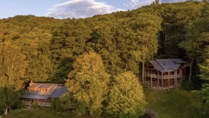 Une cabane entourée d’une forêt dense, avec une petite maison et une plus grande cabane dotée d’une terrasse.