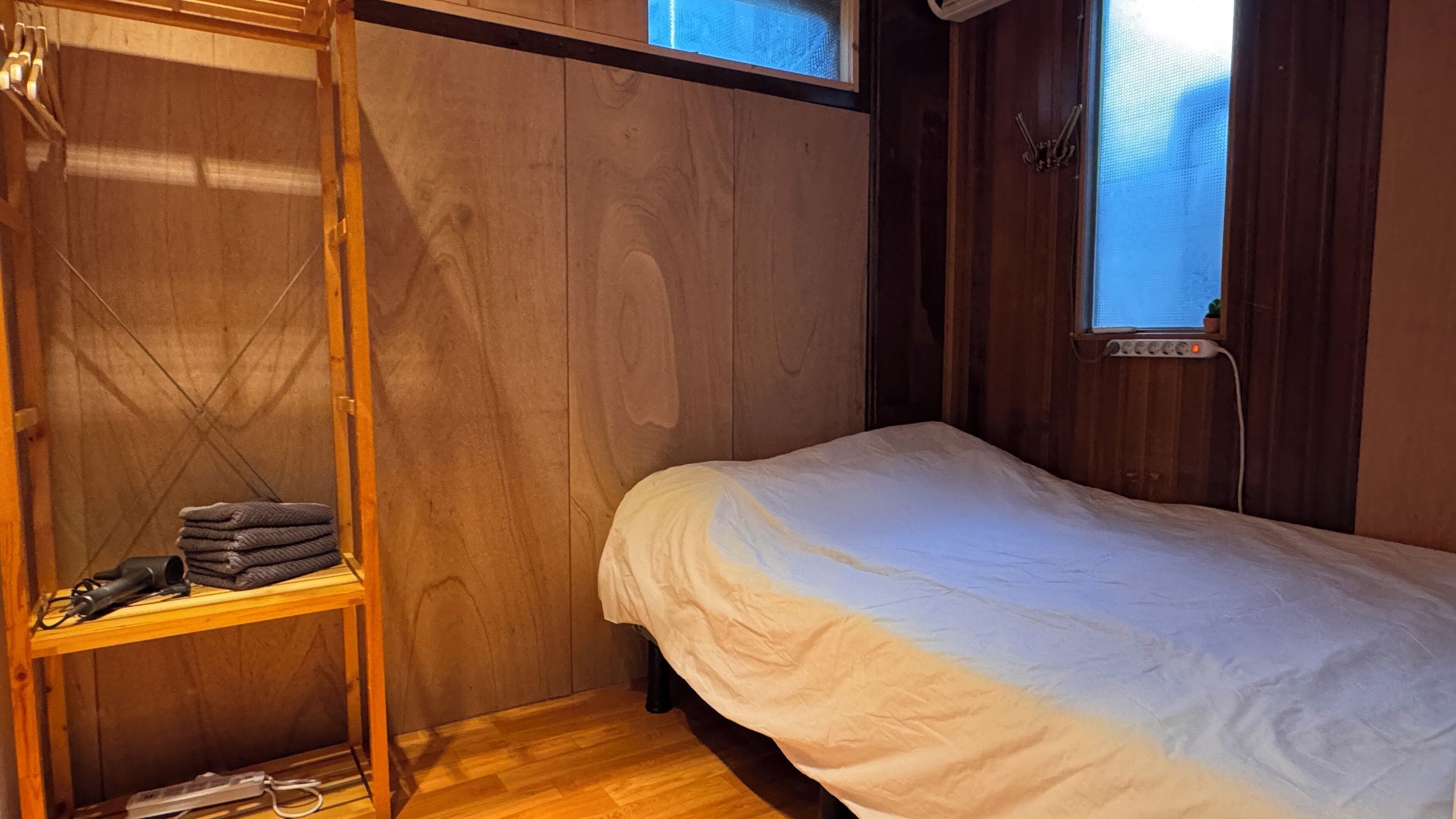 Una habitación pequeña con una cama individual y literas de madera, además de un ventanal con cortinas.