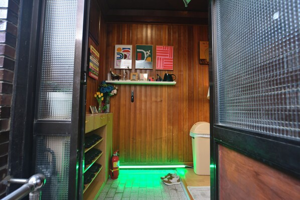 Un intérieur en bois avec une étagère où sont exposés divers objets, un extincteur et un sol éclairé en vert.