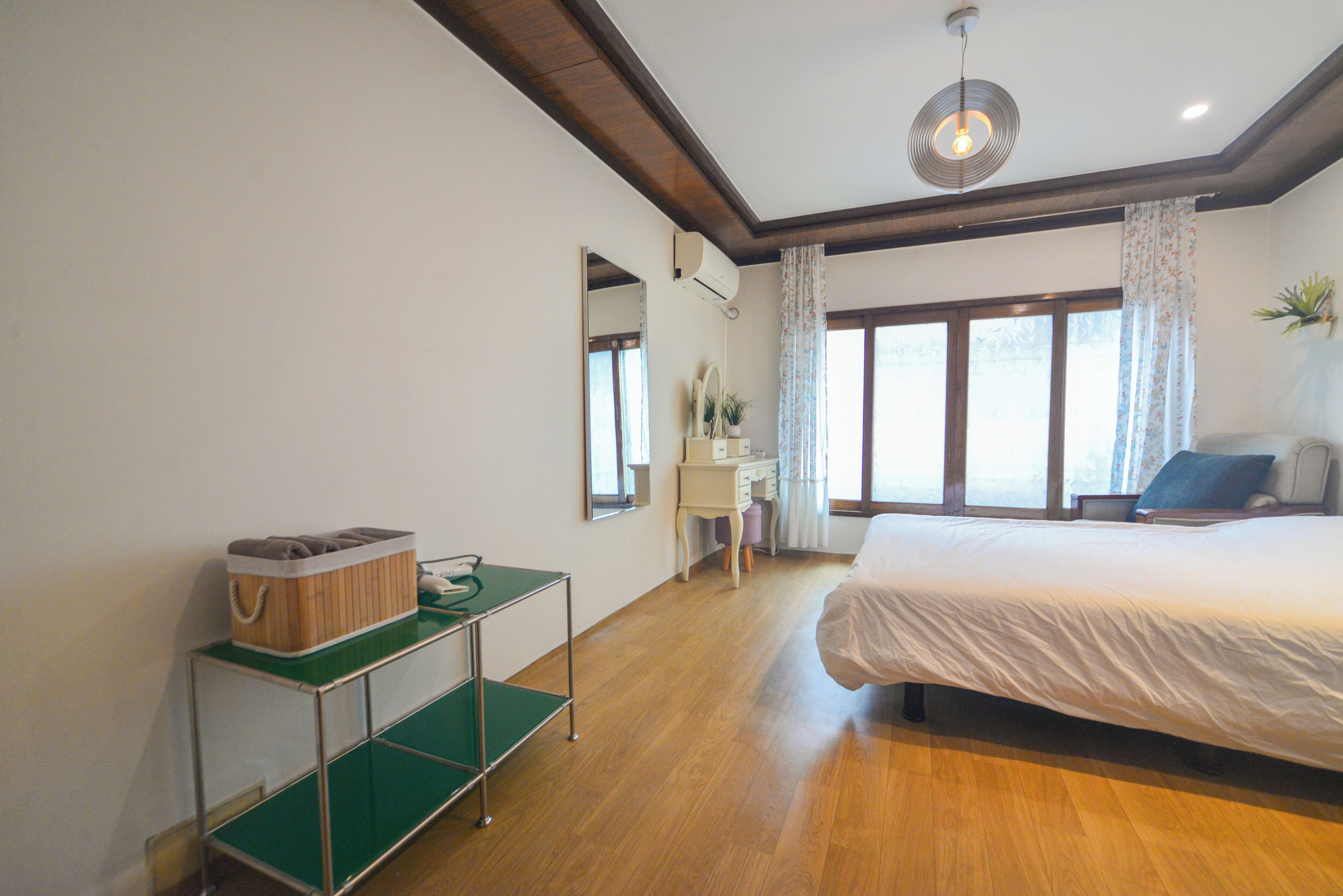 Une chambre à coucher avec un lit, un bureau, une chaise, un miroir et une fenêtre avec des rideaux.