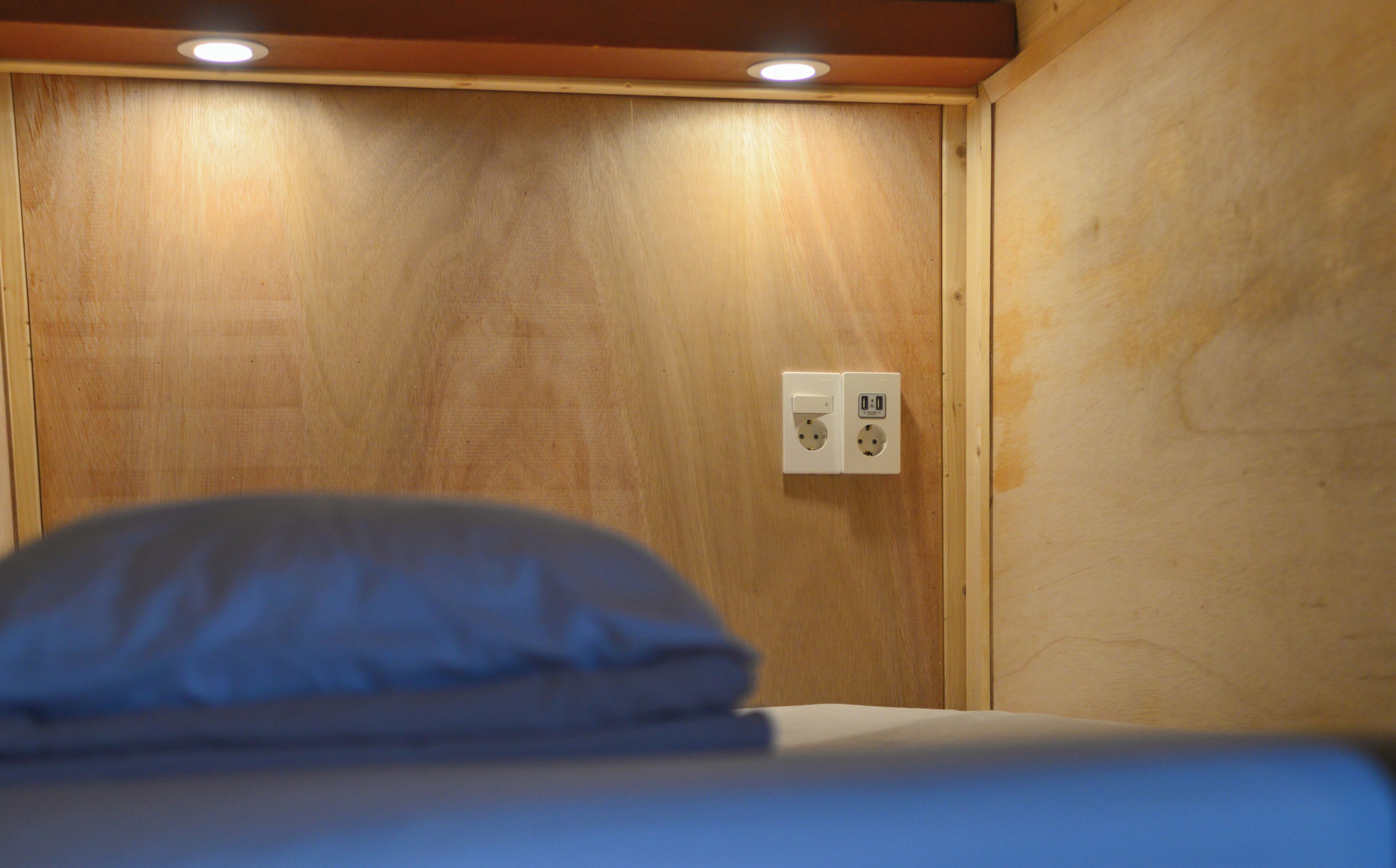 Una habitación de madera con una cama, un enchufe y un interruptor de luz.