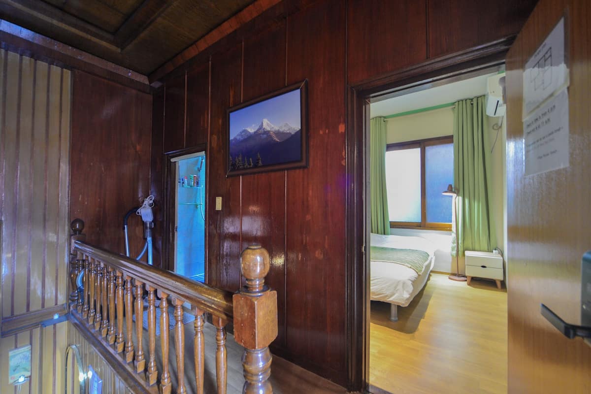 Eine Holztreppe mit Handlauf, ein gerahmtes Bild einer Berglandschaft und ein Bett in einem Zimmer mit einem grünen Vorhang.