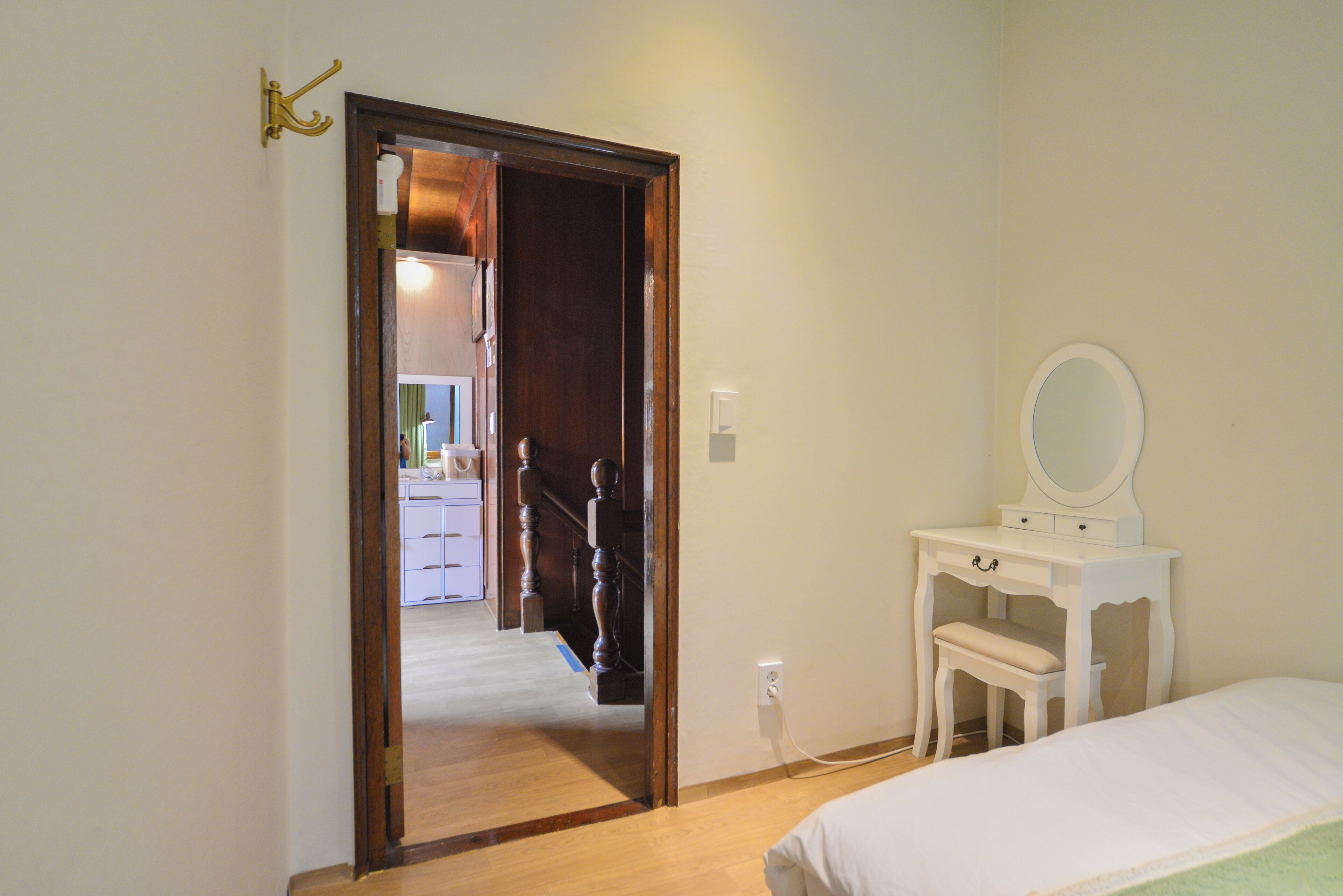 A bedroom with a wooden door leading to a hallway, a white dresser with a mirror, and a bed with a green blanket.