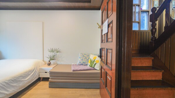 A bedroom with a bed, a small bedside table, a potted plant, and a window with a view of the outside. - Seoul Papa Guesthouse (Seoul)