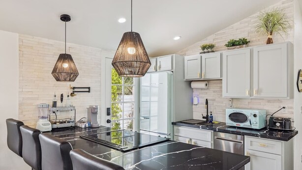 A modern kitchen with a black marble countertop, white cabinets, and two pendant lights. - Downtown Phoenix Modern Retreat | 2 Homes in 1! (Phoenix)