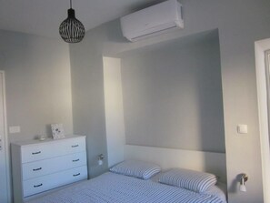 A bedroom with a bed, a dresser, a hanging light fixture, and an air conditioning unit. - Apartment AD - Pirovac (Pirovac)