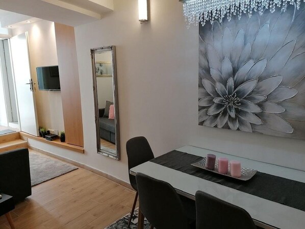 A modern living room with a large floral painting, a TV mounted on the wall, and a dining area with a table and chairs.