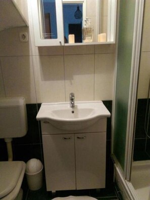 A bathroom with a white sink, a mirror above it, and a toilet to the left. - Apartment AD - Pirovac (Pirovac)