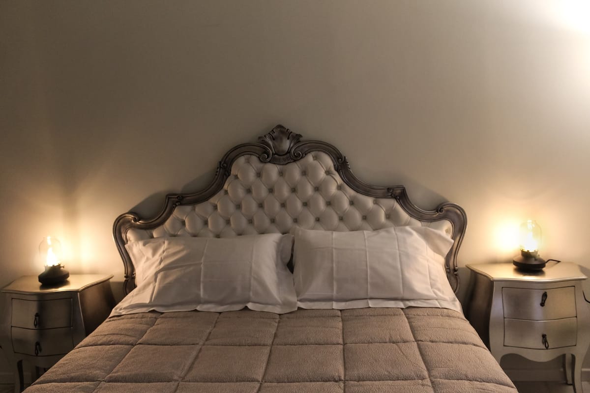 A bed with a tufted headboard, two bedside tables with lamps, and a quilted bedspread.