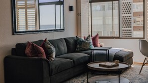 Ein modernes Wohnzimmer mit einem dunklen Sofa, einem runden Couchtisch und einem großen Fenster mit Jalousien.
