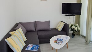 A modern living room with a grey sectional sofa, a white coffee table, and a flat-screen TV mounted on the wall. - Luxury Apartment Ani II (Sutivan)