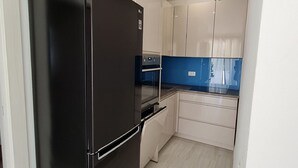 A compact kitchen with a black refrigerator, white cabinets, and a blue backsplash. - Luxury Apartment Ani II (Sutivan)