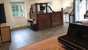 A spacious room with a wooden bed, a dining area with a table and chairs, a kitchen area, and a view of greenery outside. - La Casa d'Augy à Farges, proche de Avord et Bourges en gite de 2 à 8 personnes (Farges-en-Septaine)