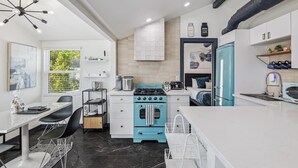 A modern kitchen with a blue stove, white cabinets, and a dining area with a table and chairs. - The Garfield Hideaway| 2BR/2BA | Walk to Downtown (Phoenix)