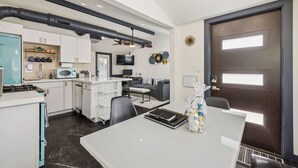 A modern kitchen with a central island, a dining area with a table and chairs, and a living space with a sofa and TV. - The Garfield Hideaway| 2BR/2BA | Walk to Downtown (Phoenix)
