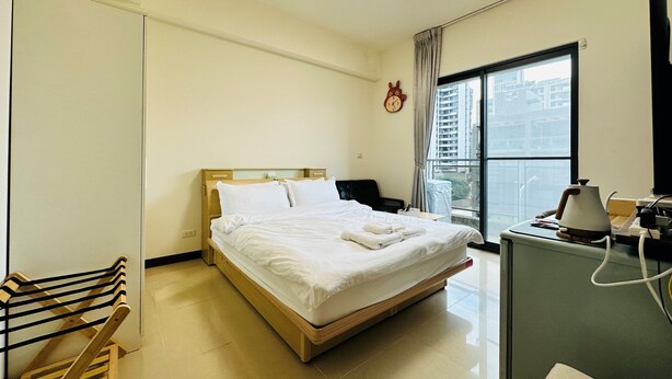 A hotel room with a bed, a desk with a lamp, a clock on the wall, and a window with a view of buildings. - Hsinchu Peace (Zhubei)