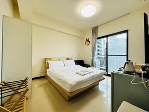 A hotel room with a bed, a desk with a lamp, a clock on the wall, and a window with a view of buildings. - Hsinchu Peace (Zhubei)