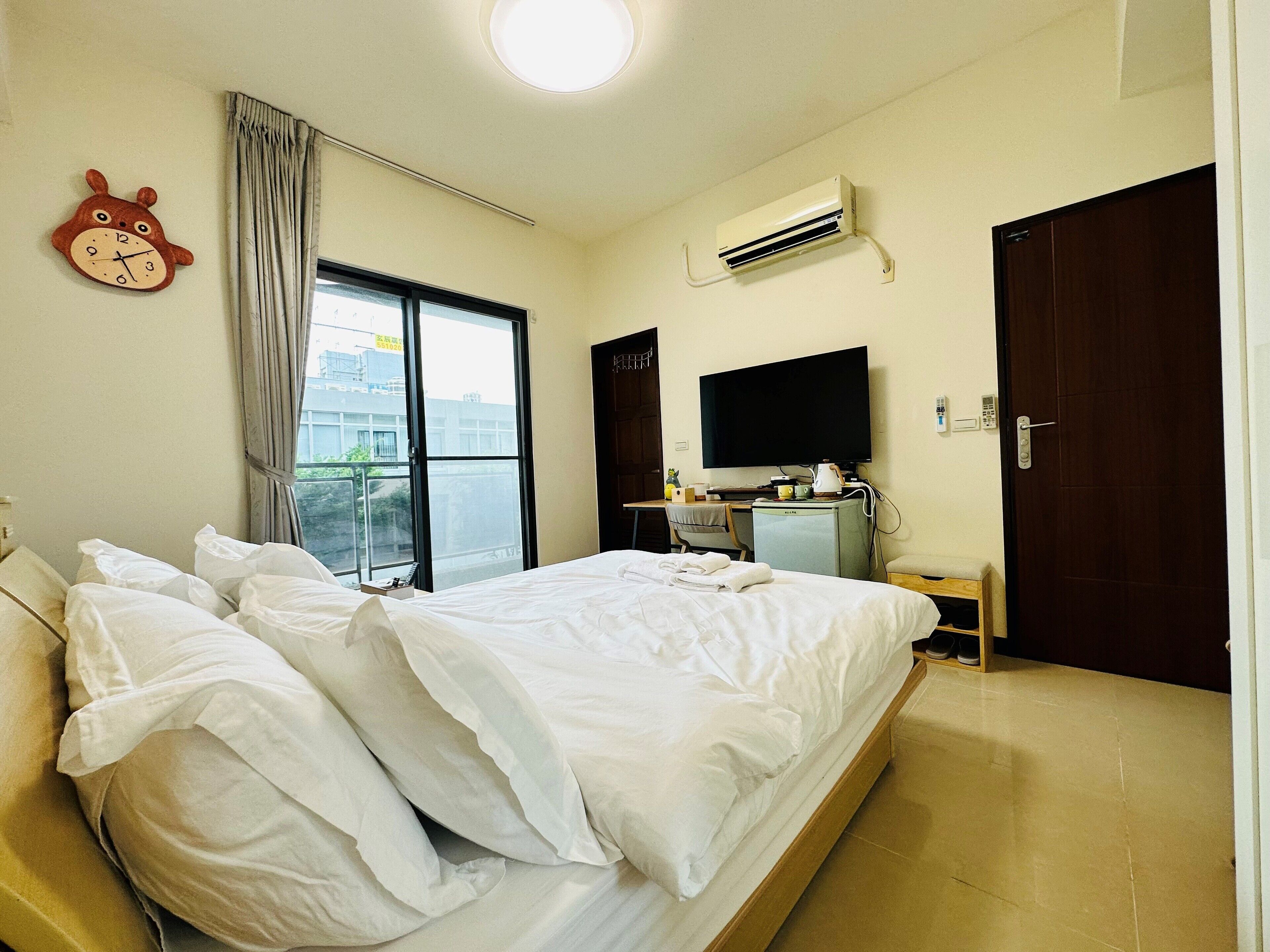 A hotel room with a bed, a desk with a computer, an air conditioner, a TV, and a window with curtains.