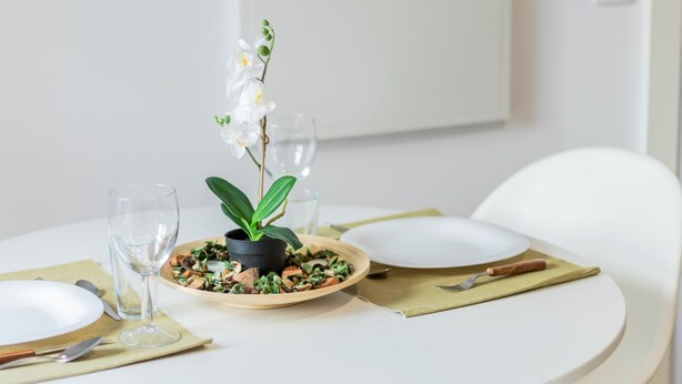 Ein Esstisch mit einer Salatschale, einer Topf-Orchidee und Weingläsern.