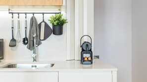 A modern kitchen with a stainless steel sink, hanging utensils, a potted plant, and a portable gas stove.