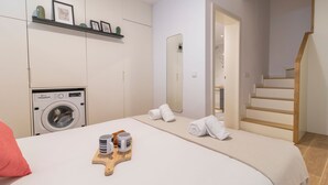Ein Schlafzimmer mit Waschmaschine, einem Bett mit Handtüchern, einem Holztablett mit Tassen und einer Treppe.
