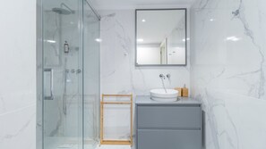 Bathroom features a glass-enclosed shower, handheld showerhead, and wall-mounted faucet.