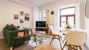 Ein modernes Wohnzimmer mit einem grünen Sofa, einem Flachbildfernseher, einem Esstisch mit Stühlen und gerahmten Bildern an der Wand.