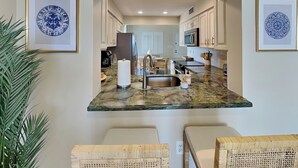 A kitchen with a marble countertop, two wicker chairs, and framed artwork on the walls.