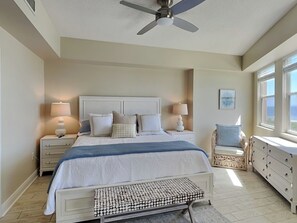 A bedroom with a bed, bedside tables, a chair, a dresser, a ceiling fan, and a window. - Surf Club by VTrips (Palm Coast)