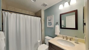 A bathroom with a shower curtain, toilet, sink, and mirror. - Surf Club by VTrips (Palm Coast)